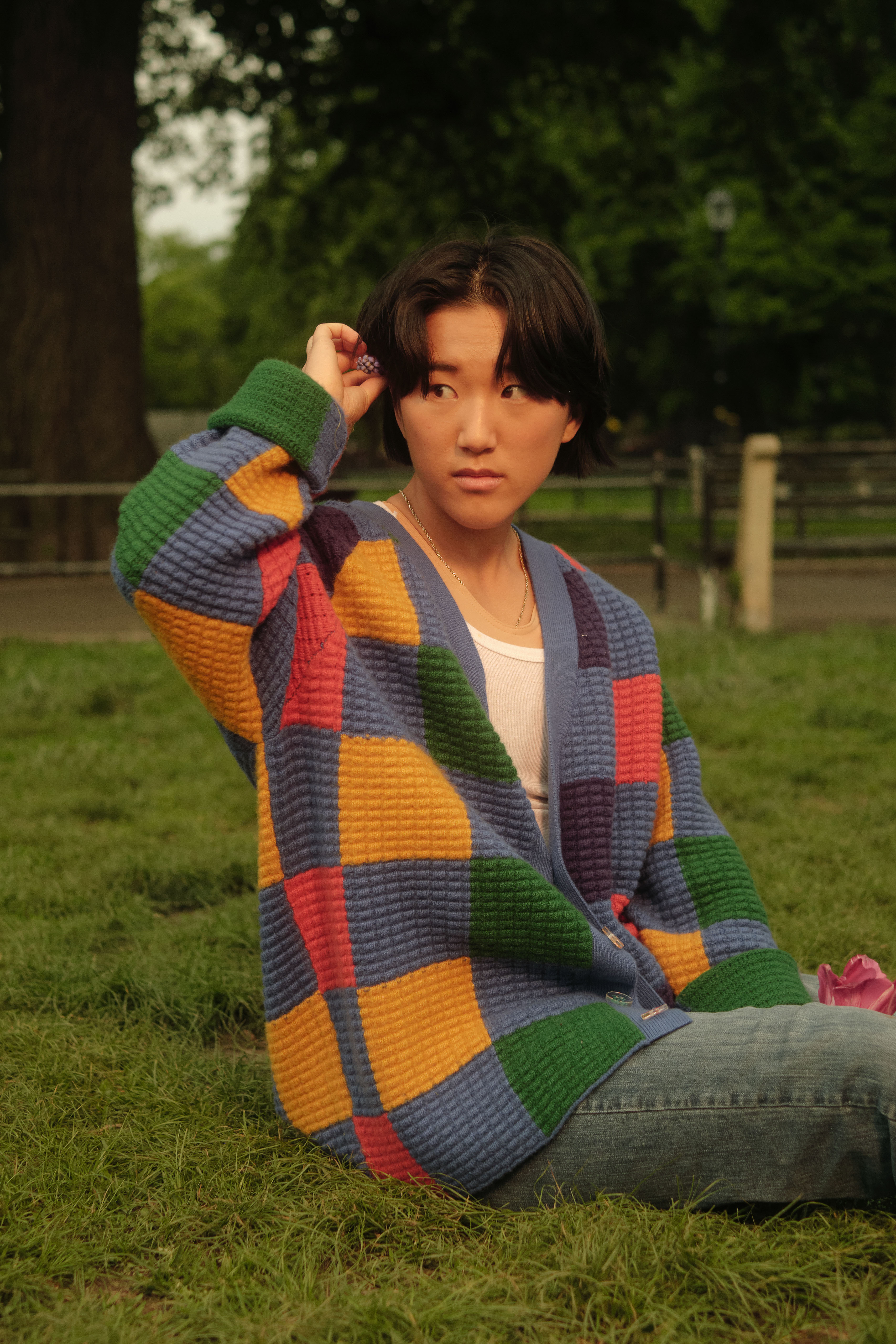 A non-binary trans man sitting on grass, holding a flower(1)